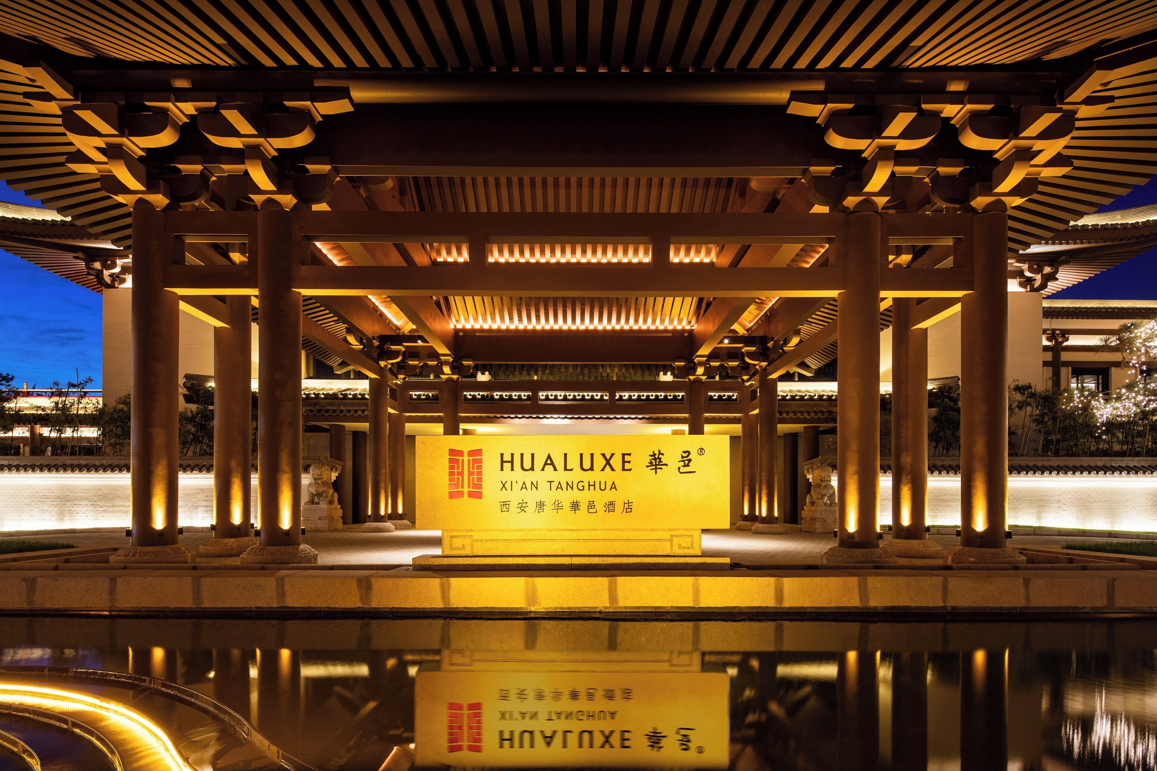 A traditional pavilion with illuminated pillars and a reflective pool in front.