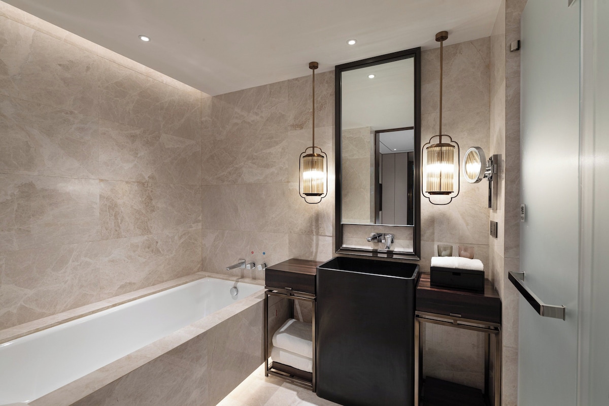 A modern bathroom with a freestanding bathtub, a dark vanity, and two wall-mounted sconces.