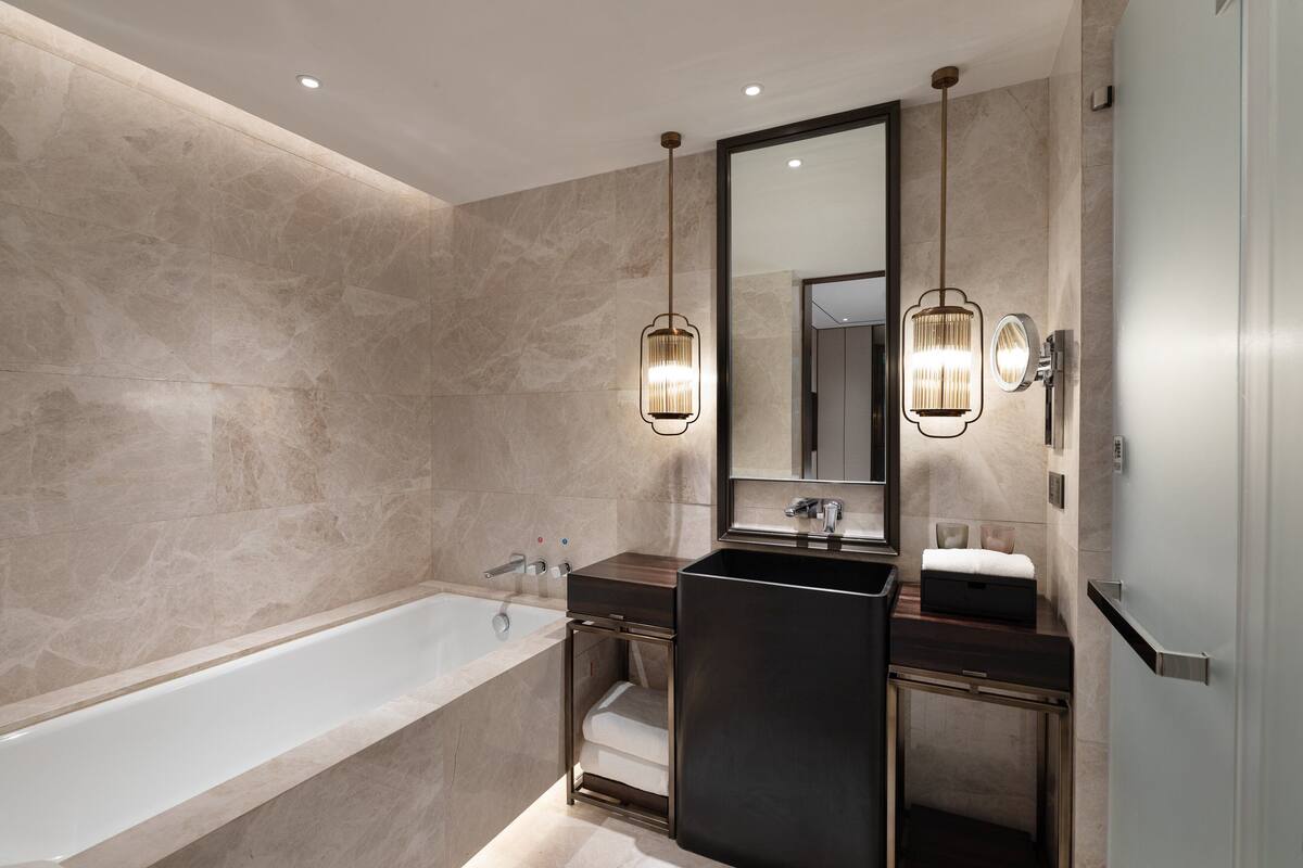 Un baño moderno con una bañera grande, un tocador oscuro y dos lámparas colgantes.