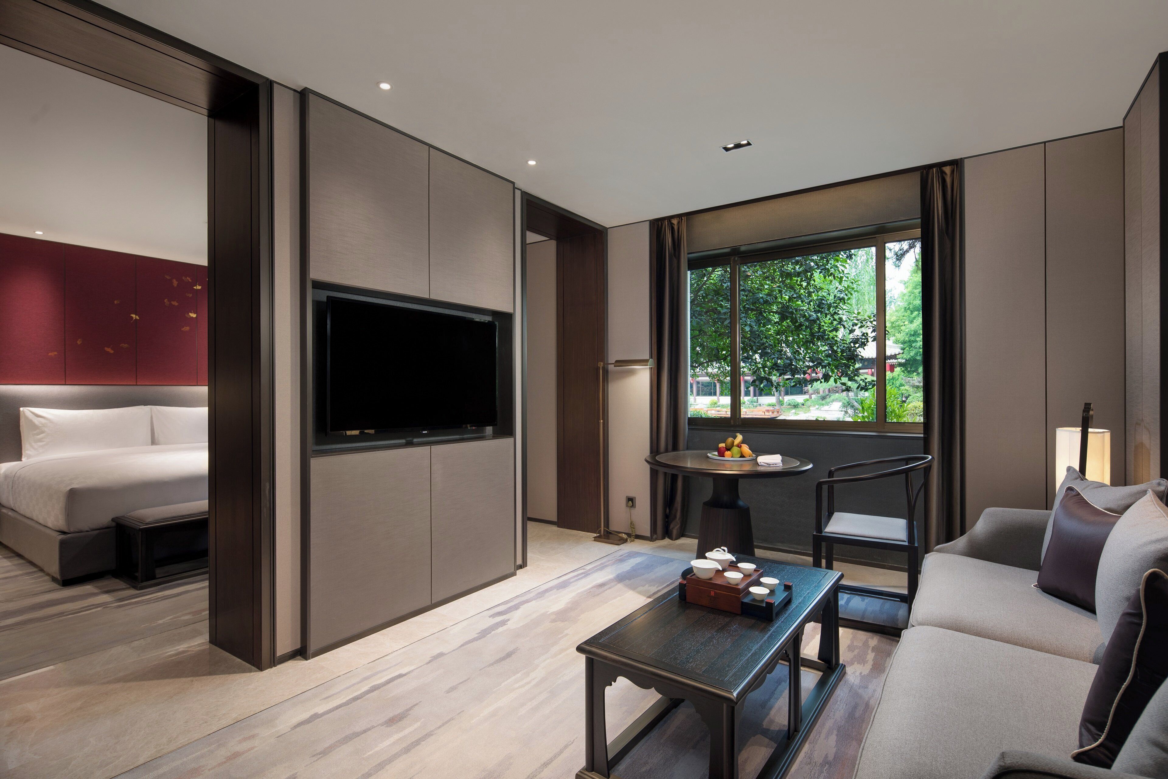 Una habitación de hotel moderna con una cama, un televisor de pantalla plana, una mesa de comedor con frutero y un sofá.