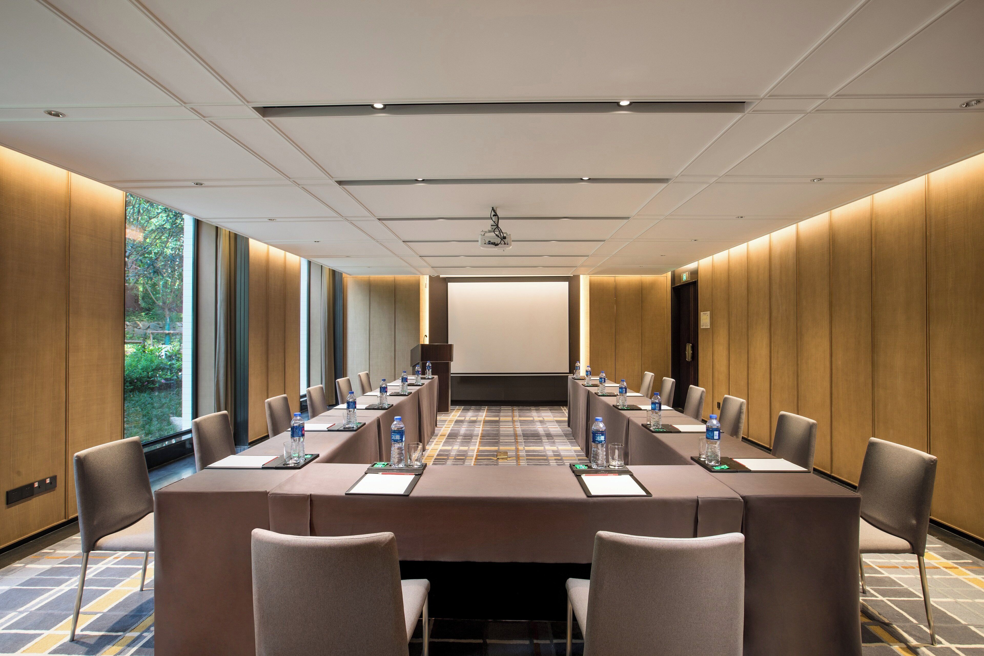 A conference room with a long table, chairs, water bottles, and a projector screen.