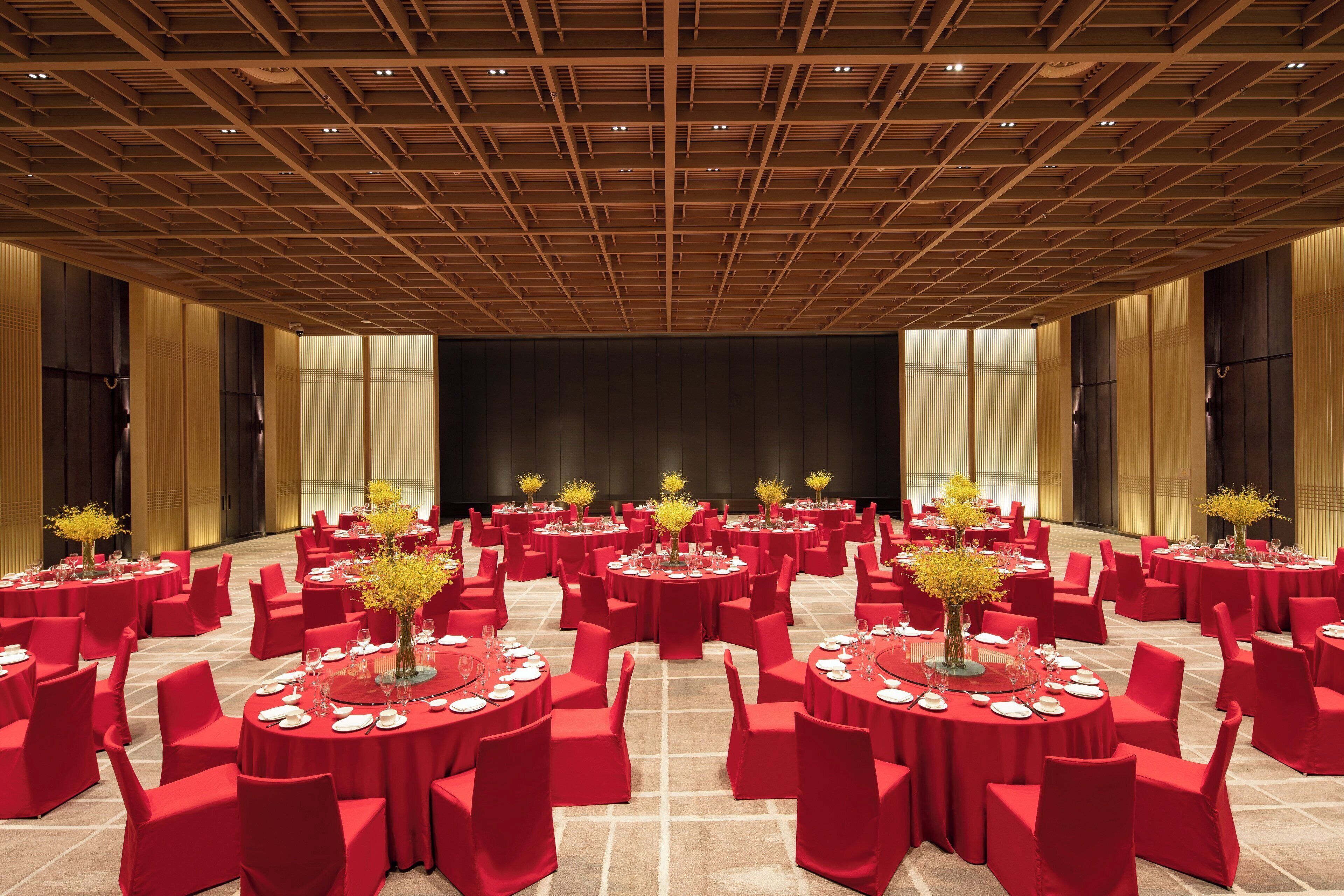 Un amplio salón con mesas redondas, sillas rojas y arreglos florales amarillos.