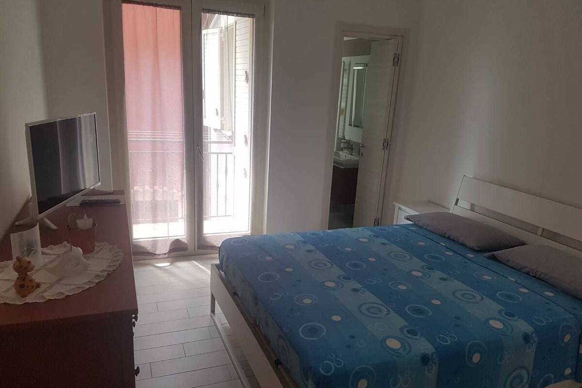 A bedroom with a bed, a TV, a desk, and a sliding glass door to the outside.