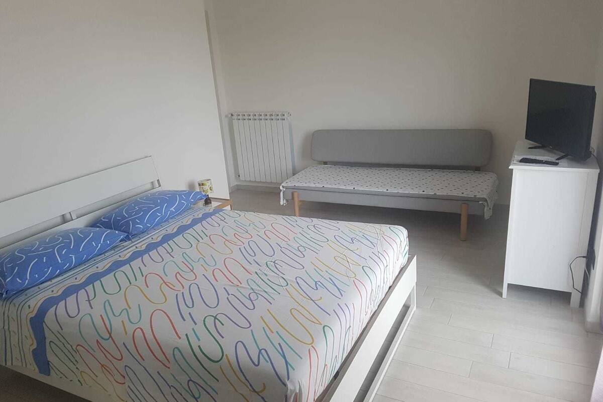 A bedroom with a bed, a bench, a TV, and a radiator.