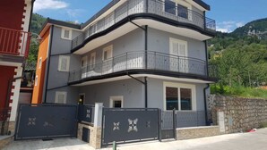 Un edificio residencial de varios pisos con balcones, una entrada vigilada y montañas al fondo.