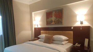 Une chambre d’hôtel avec un grand lit, deux lampes de chevet, un tableau au mur et une table de chevet avec un téléphone et un panneau.