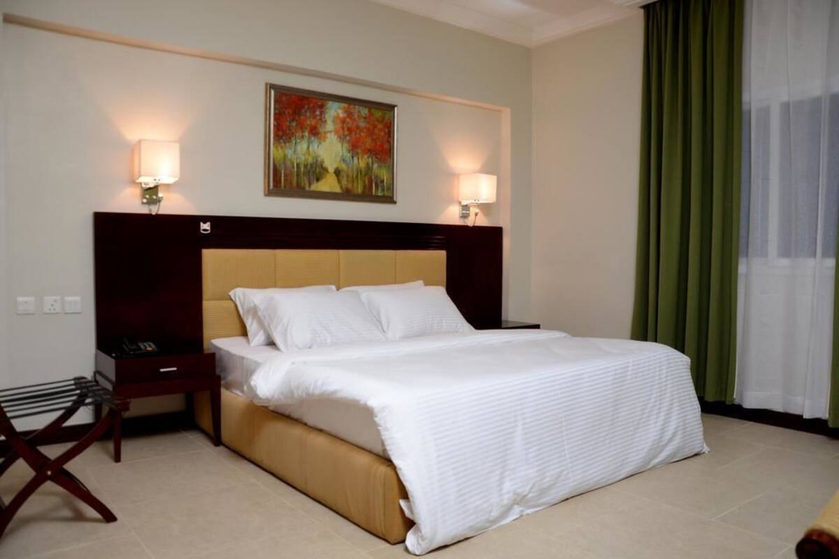 Ein Hotelzimmer mit einem großen Bett, zwei Nachttischen, einem Kopfteil und einem Gemälde an der Wand.