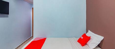 A bedroom with a bed, a red and white bedspread, a red pillow, and a television on the wall.