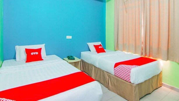 Une chambre d’hôtel avec deux lits, chacun recouvert d’une courtepointe rouge et blanche, et un mur vert.