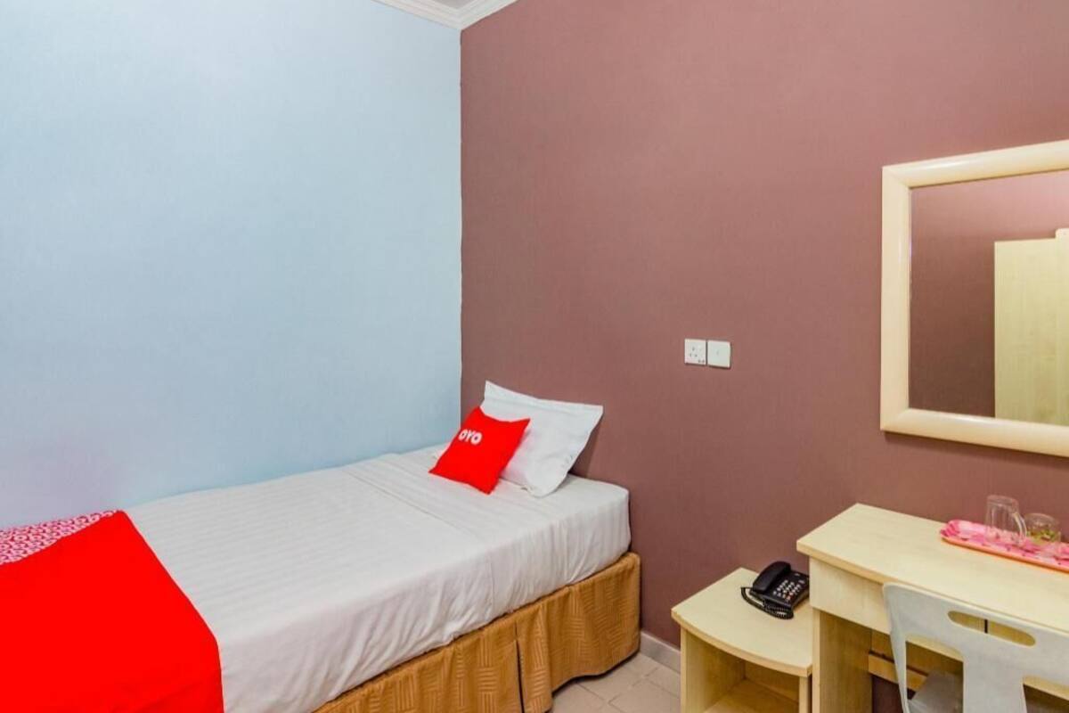 Een eenpersoonsbed met een rood kussen, een bureau met telefoon en een spiegel aan de muur.