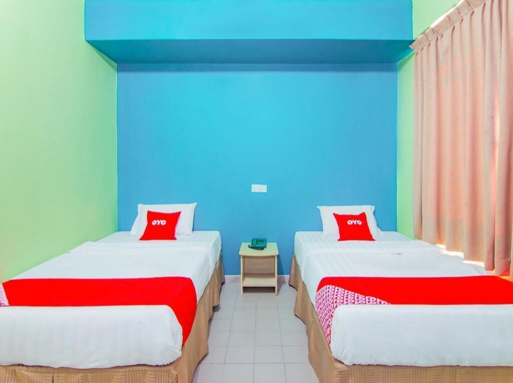 Ein Zimmer mit zwei Betten, jeweils mit einem roten Kissen, einem kleinen Tisch und einer blauen Wand.