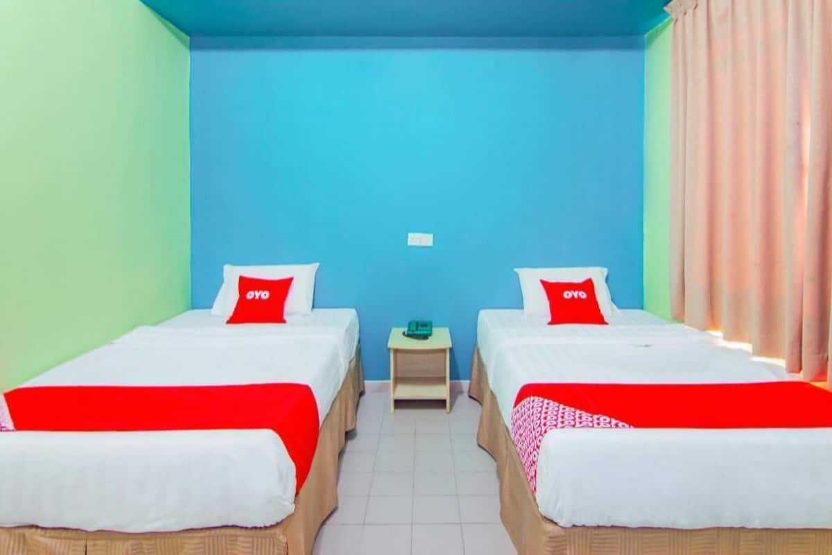 A room with two beds, each with a red pillow, a small table, and a blue wall.