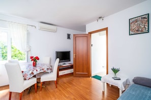 Una habitación con piso de madera, una mesa de comedor con sillas, un televisor, una puerta de madera y un cuadro en la pared.