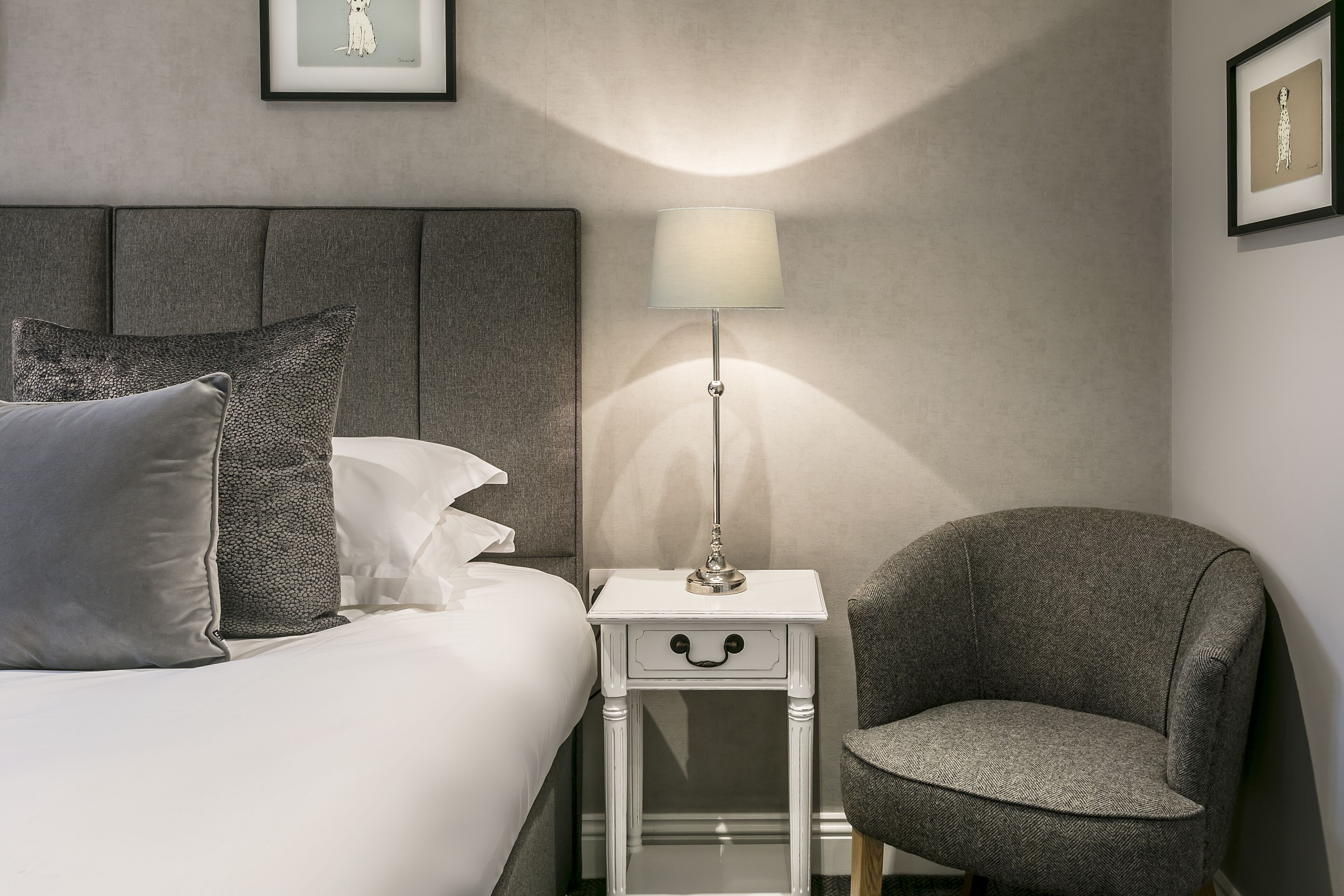 Habitación de hotel ordenada con una cama, una mesita de noche con lámpara y un sillón gris.