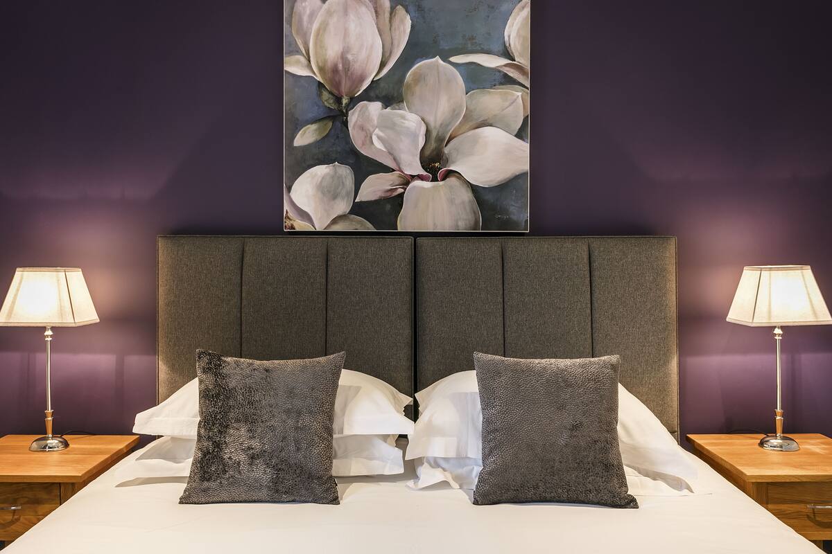 A hotel room with a large bed, two nightstands, and a wall-mounted painting of flowers.