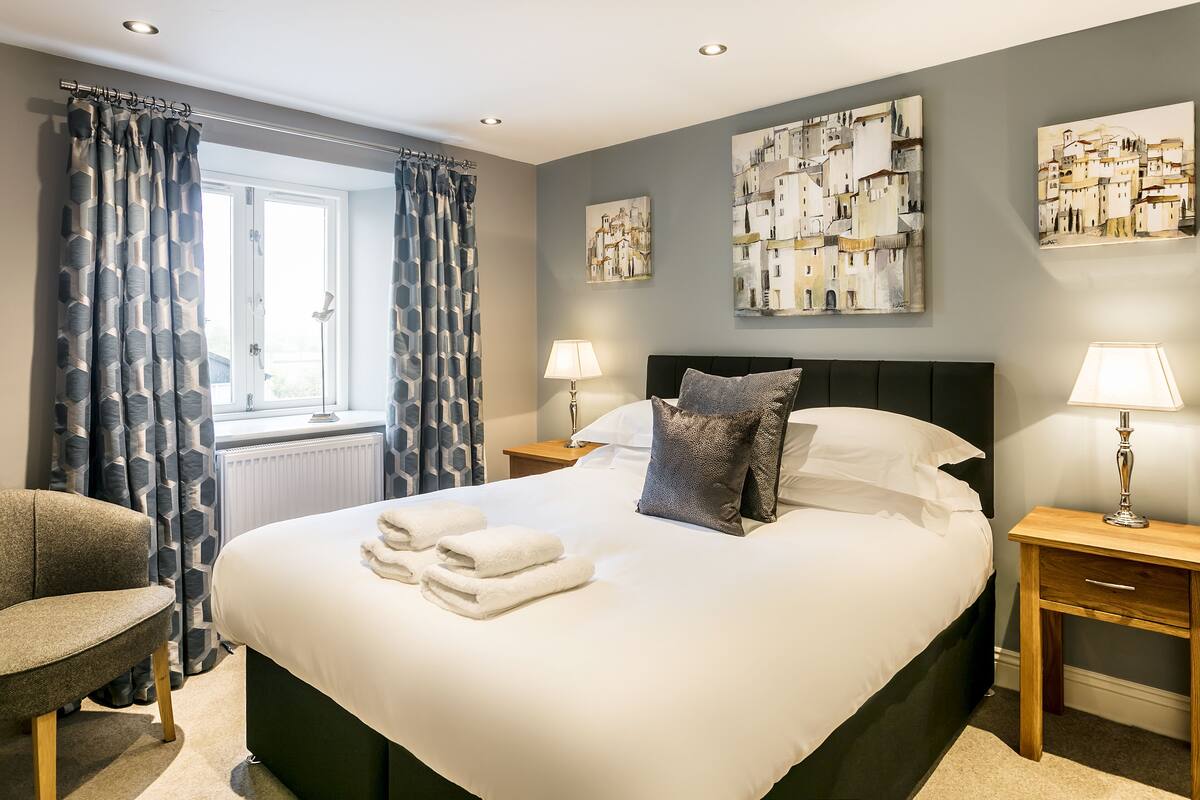 A neatly made bed with white linens and towels, a bedside lamp, and a chair.