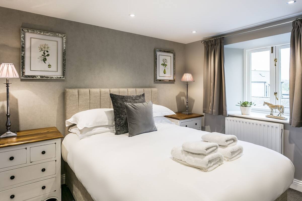 A neatly arranged bedroom with a bed, bedside tables, lamps, and framed botanical prints on the wall.