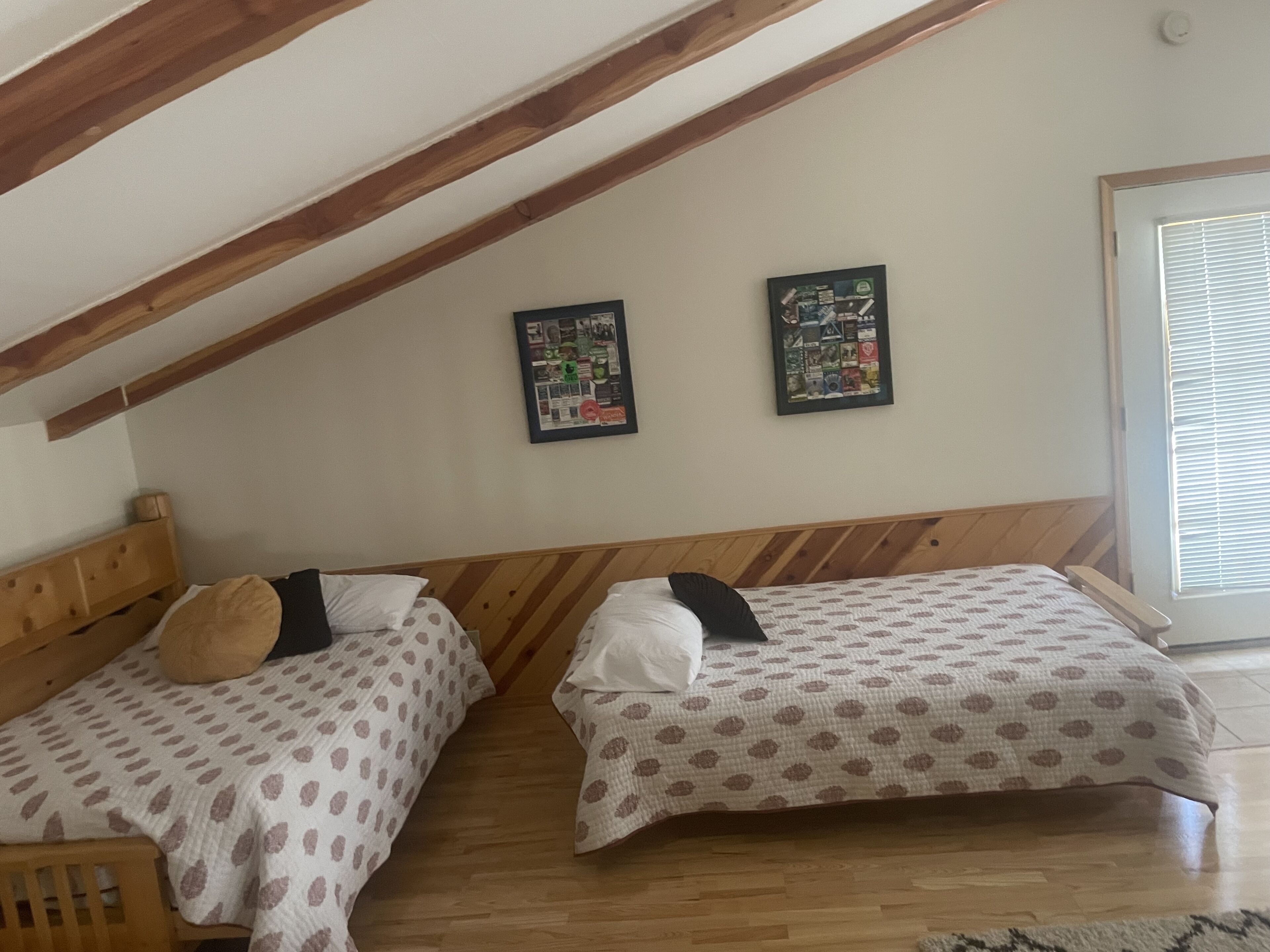 A bedroom with two beds, wooden headboards, a sloped ceiling, and two framed posters on the wall.