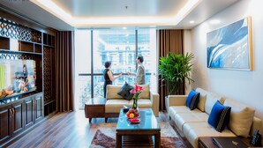 A modern hotel room with a TV, sofa, coffee table, and a large window offering a city view. - Menrva Hotel (Hai Phong)
