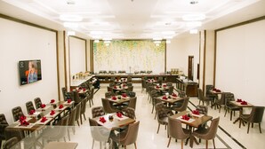 A spacious conference room with multiple tables and chairs, a large screen, and a decorative wall. - Menrva Hotel (Hai Phong)