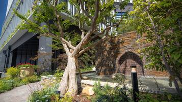 A modern building with a large tree in the courtyard, a brick archway, and a water feature.