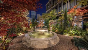 A circular water feature with a fountain in the center, surrounded by a brick pathway and various plants. - Hotel Trad Hakata (Fukuoka)