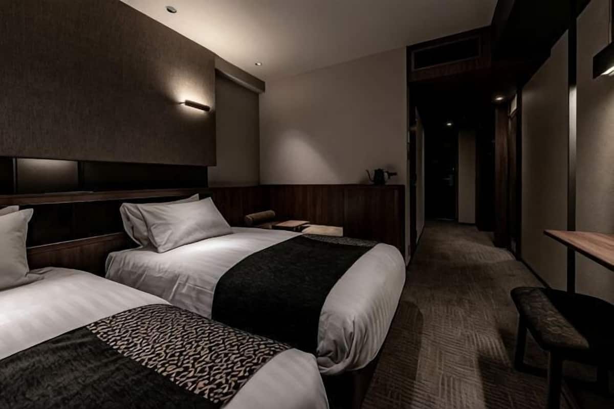 A hotel room with two beds, a bench, a desk, and a walk-in closet.