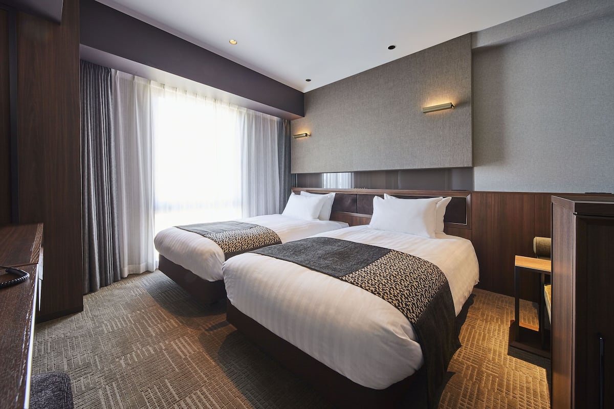 A hotel room with two beds, a desk, and a large window with curtains.