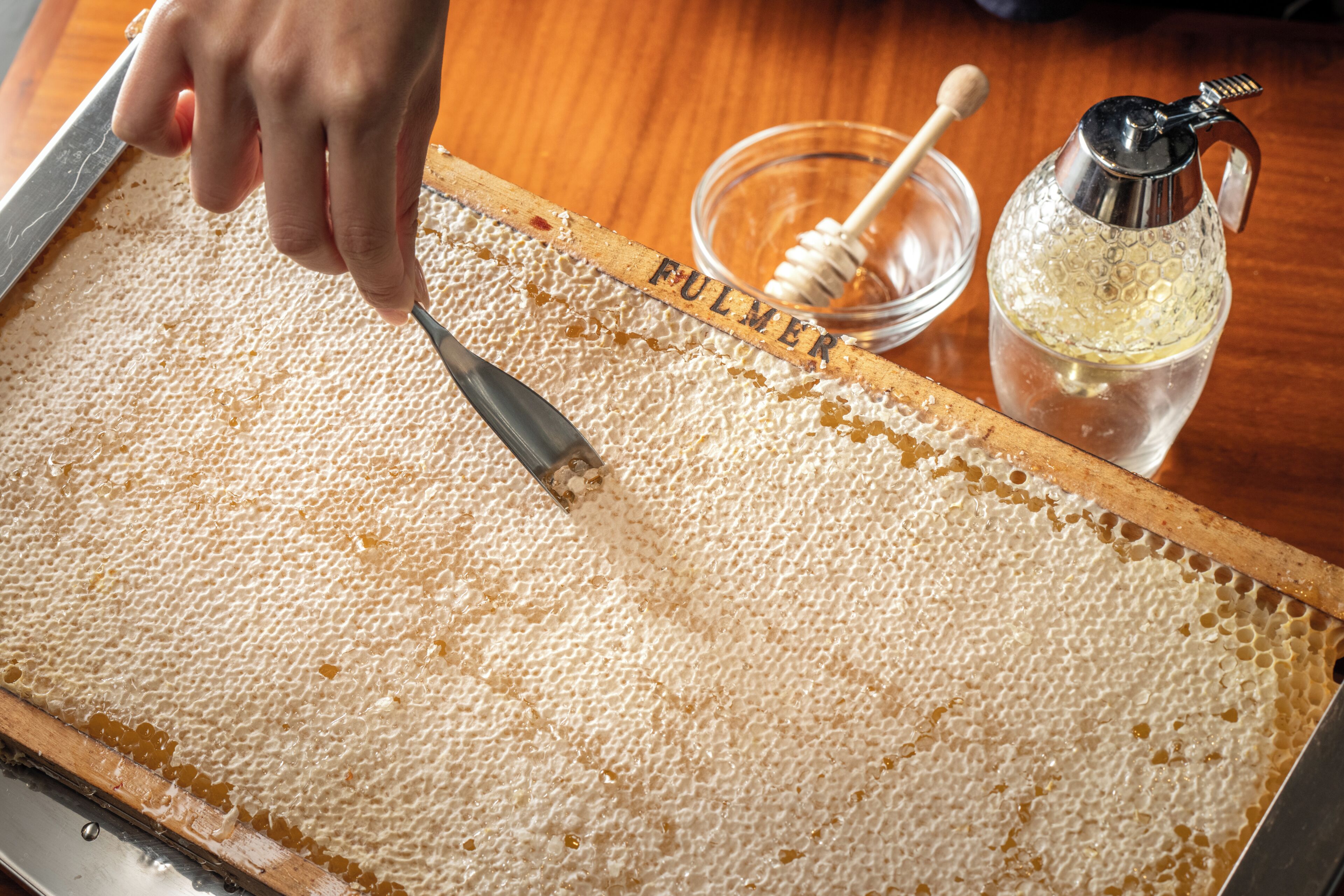 A honeycomb frame with the word 'FULMER' on it, a honey dipper, and a honey jar.
