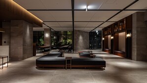 A modern lobby with a central seating area, stone walls, and a view of greenery outside. - Hotel Trad Hakata (Fukuoka)