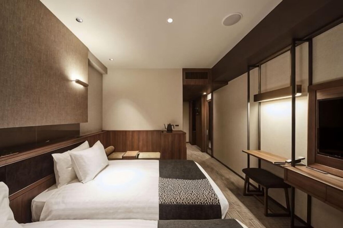 A hotel room with a large bed, a desk, a bench, and a television.
