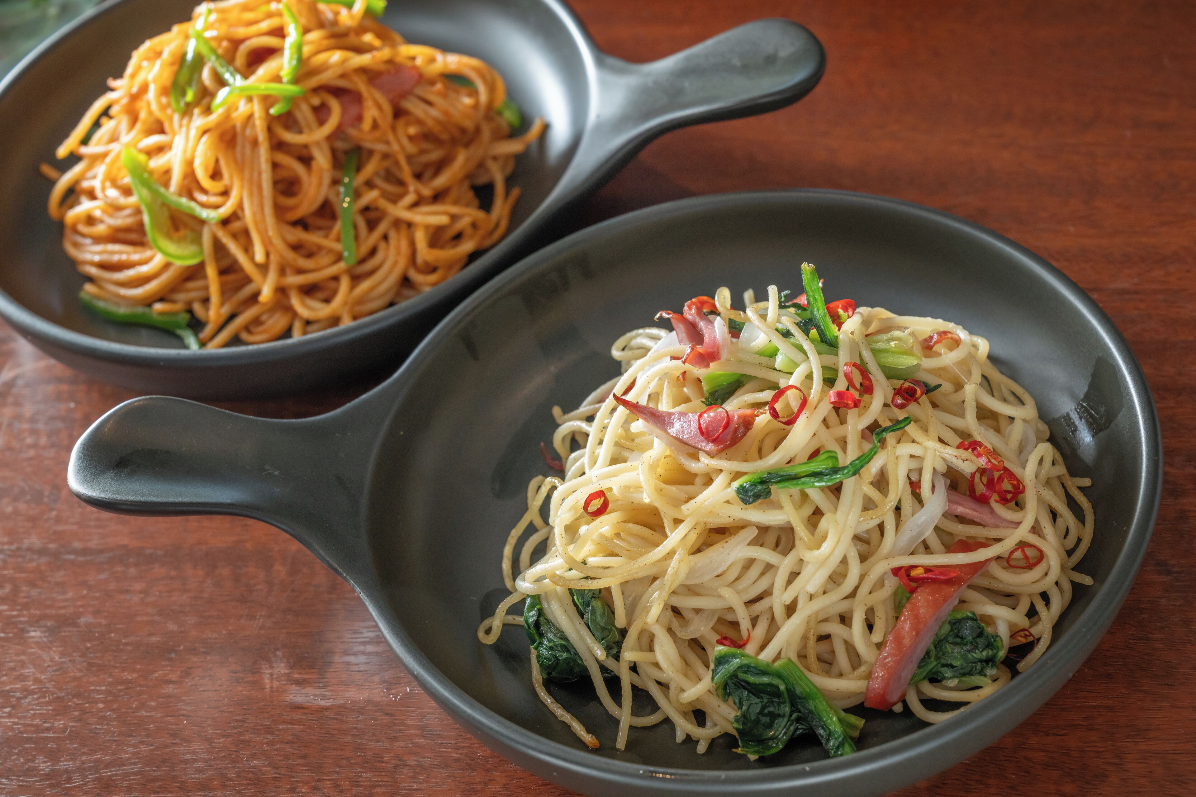Two bowls of noodles with different toppings on a wooden table.