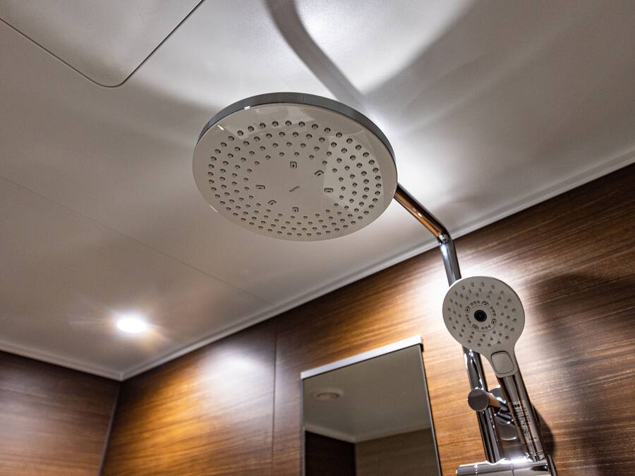 A modern bathroom with a shower head, wooden wall paneling, and a mirror.