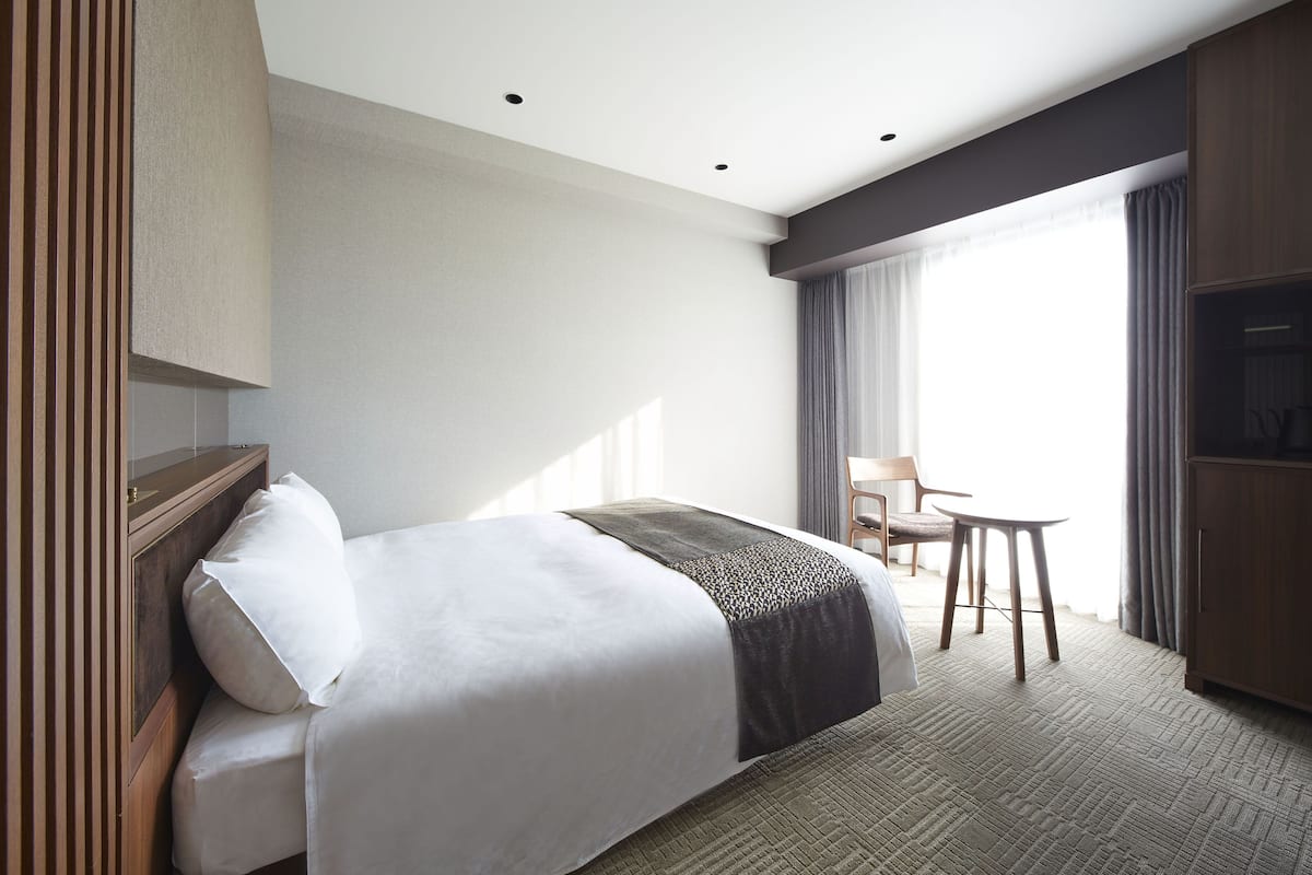 A hotel room with a large bed, a desk, a chair, a television, and a window with curtains.