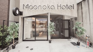 Exterior de l'Hotel Moonoka, amb disseny modern, que destaca una entrada de vidre i plantes en testos.