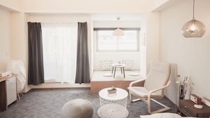 Un saló modern amb un sofà, una cadira de fusta, una taula rodona petita i una planta decorativa.