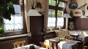 Un comedor acogedor con mesas y sillas de madera, cortinas de encaje y lámparas colgantes.
