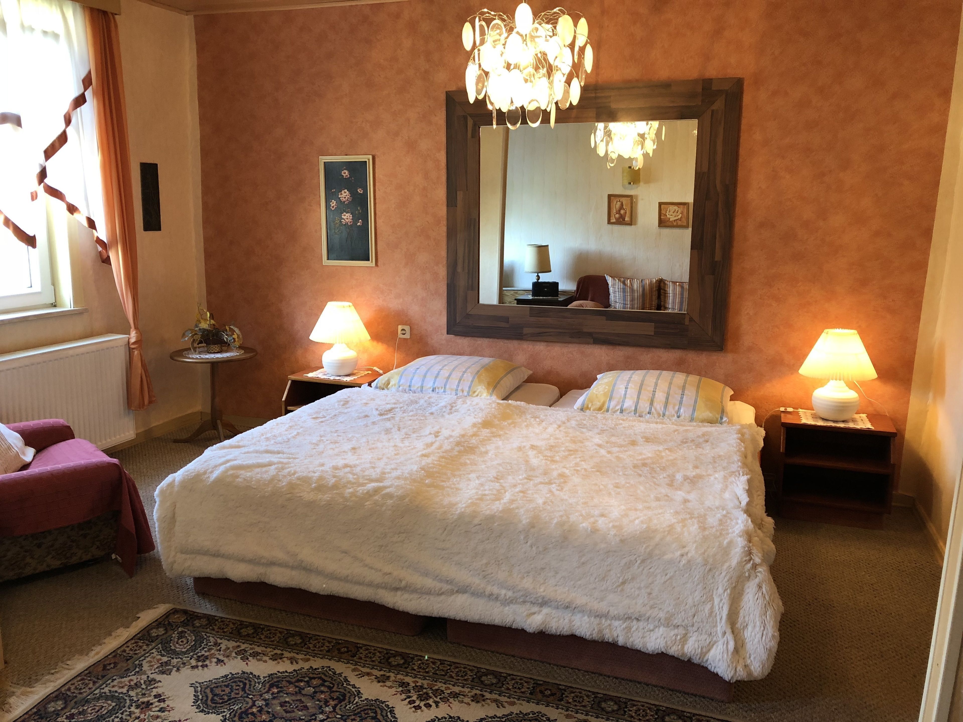 Une chambre à coucher avec un grand lit, deux lampes de chevet, un lustre, un miroir et une petite table avec une lampe.