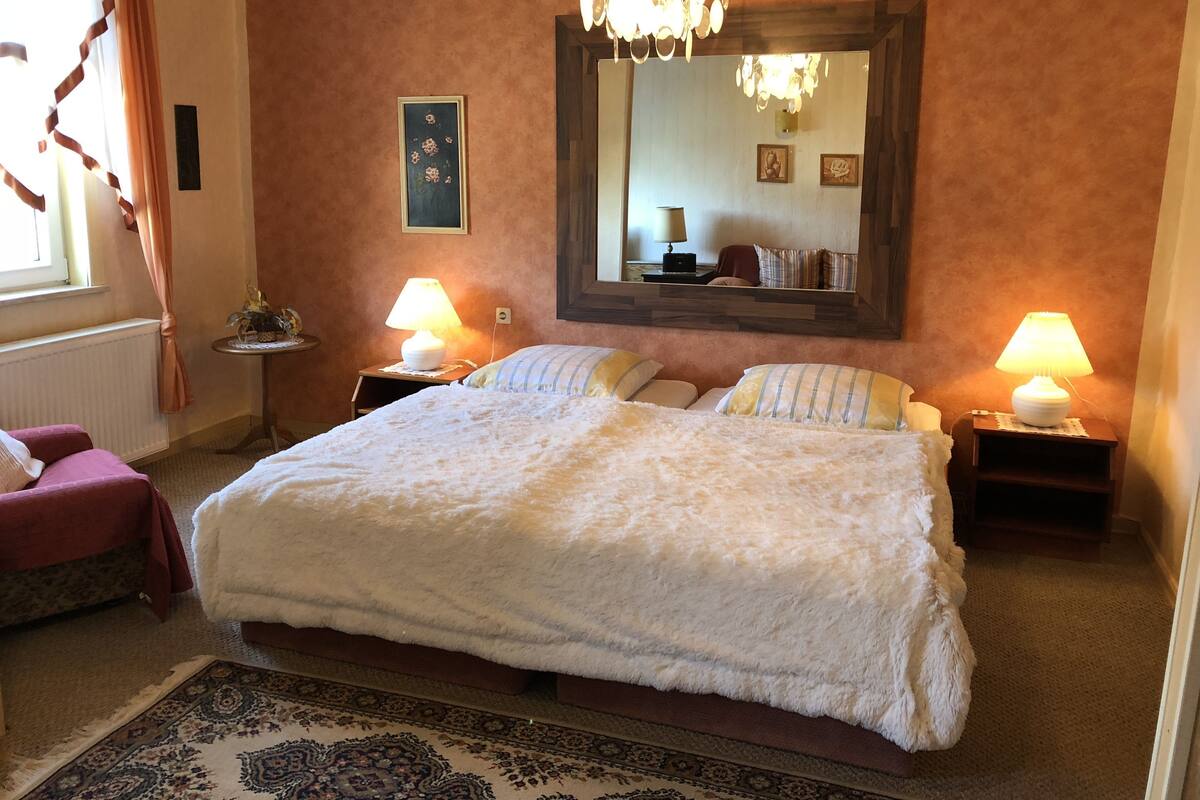 Un dormitori amb un llit gran, dues làmpades de nit, una pèndol, un mirall i una taula petita amb una làmpada.