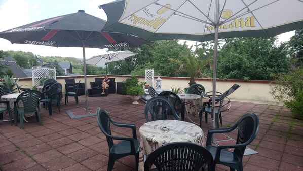 An outdoor patio with tables and chairs, umbrellas, and potted plants.