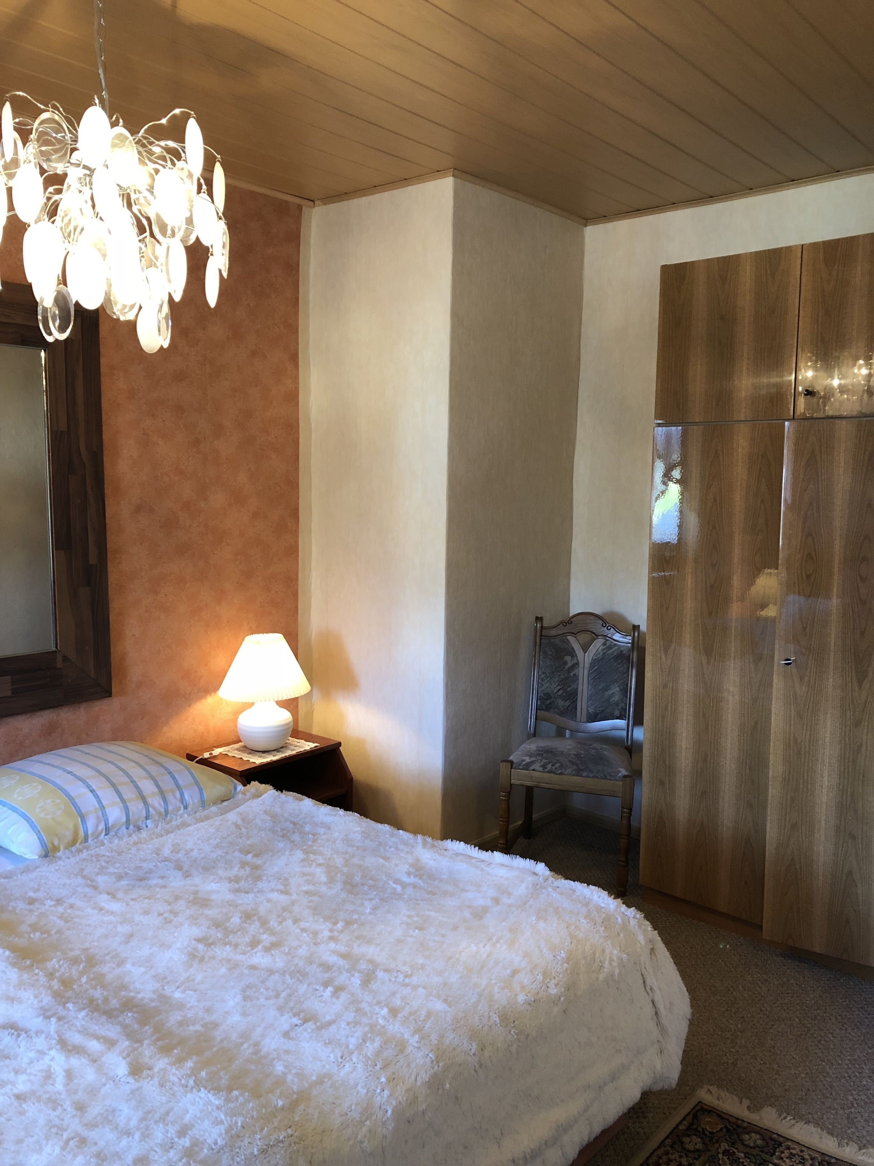Una camera da letto con un letto, una sedia, un armadio in legno, una lampada e un lampadario.