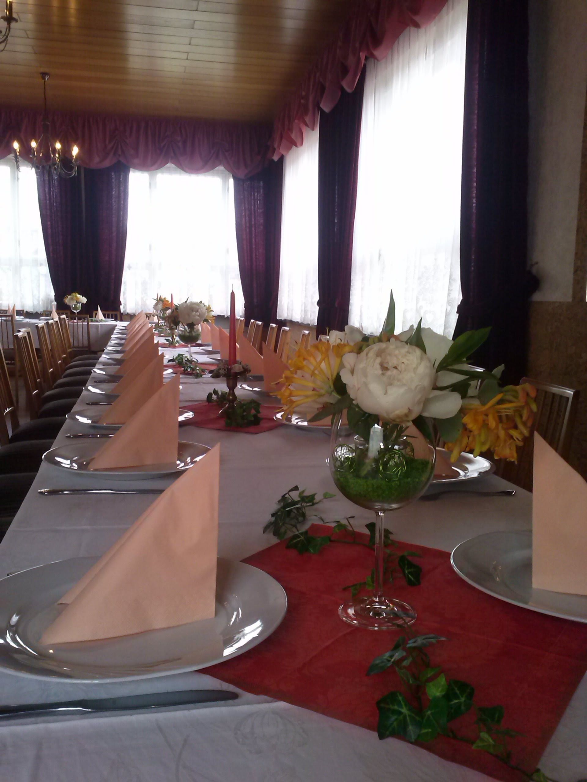 Une longue table à manger, dressée avec des assiettes, des serviettes et un centre de table agrémenté de fleurs et de verdure.