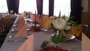Une longue table à manger, dressée avec des assiettes, des serviettes et un centre de table agrémenté de fleurs et de verdure.