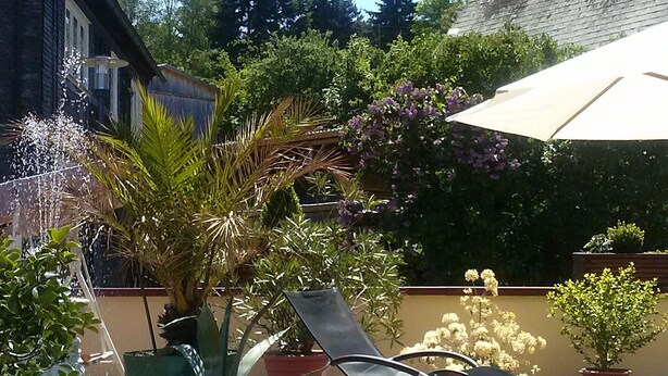 Un patio al aire libre con una silla de descanso, un gran paraguas y plantas en macetas.