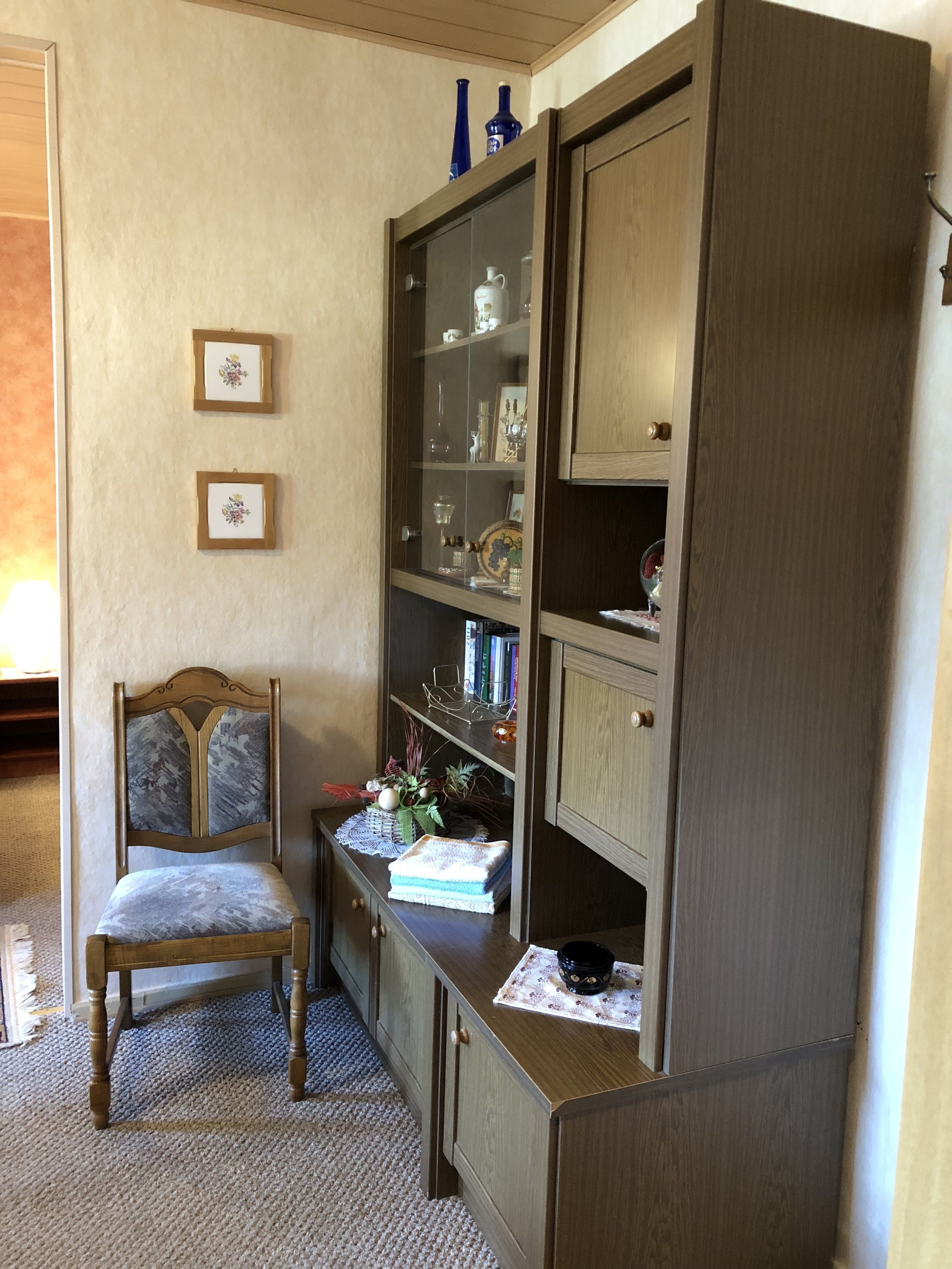 A room with a wooden cabinet, a chair, and two framed pictures on the wall.