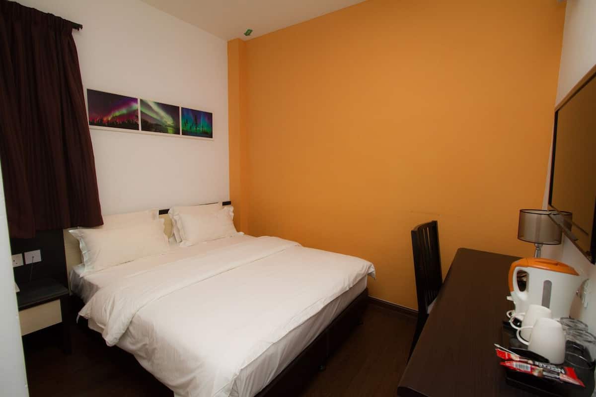 A hotel room with a bed, a desk with a coffee maker, and a wall with three pictures.