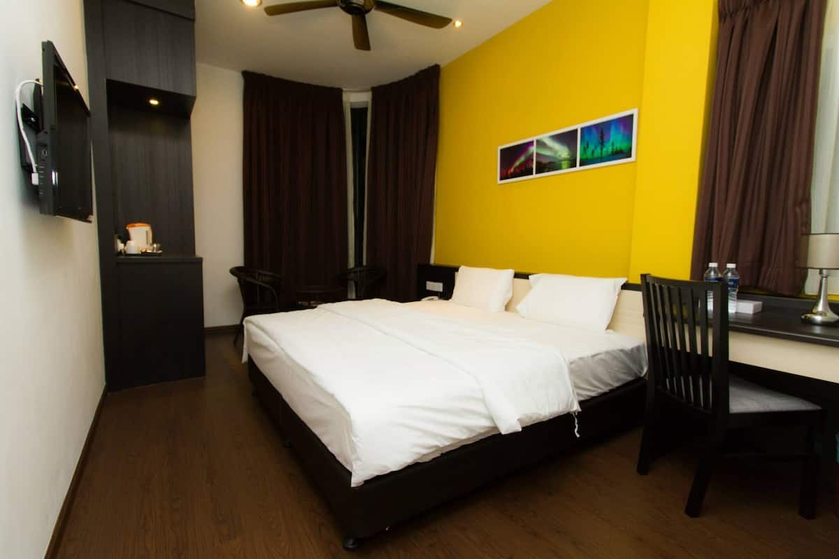 A hotel room with a bed, a desk, a chair, a TV, and a coffee machine.