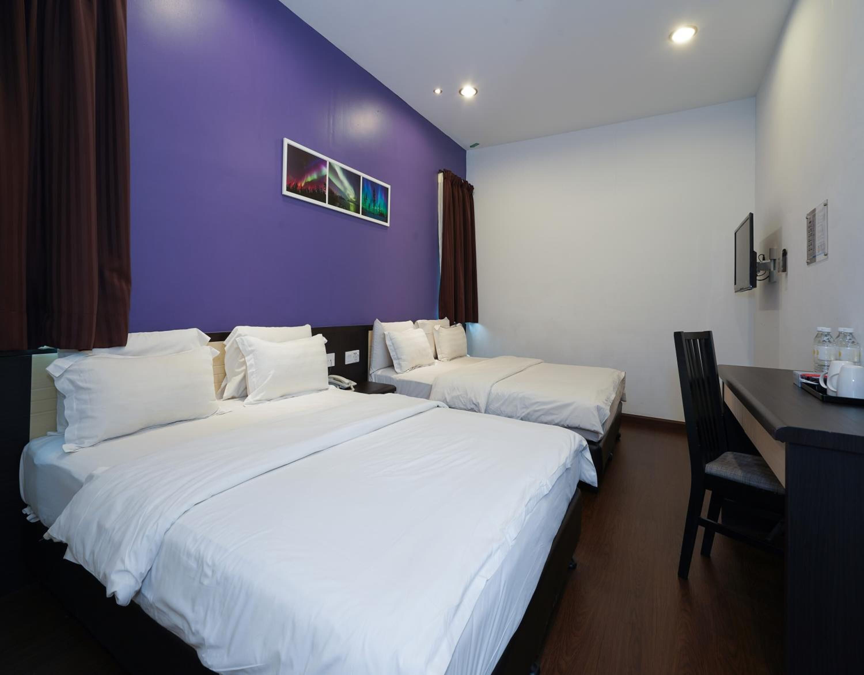 A hotel room with two beds, a desk, and a chair. There are curtains on the windows, and a picture of the Northern Lights on the wall.