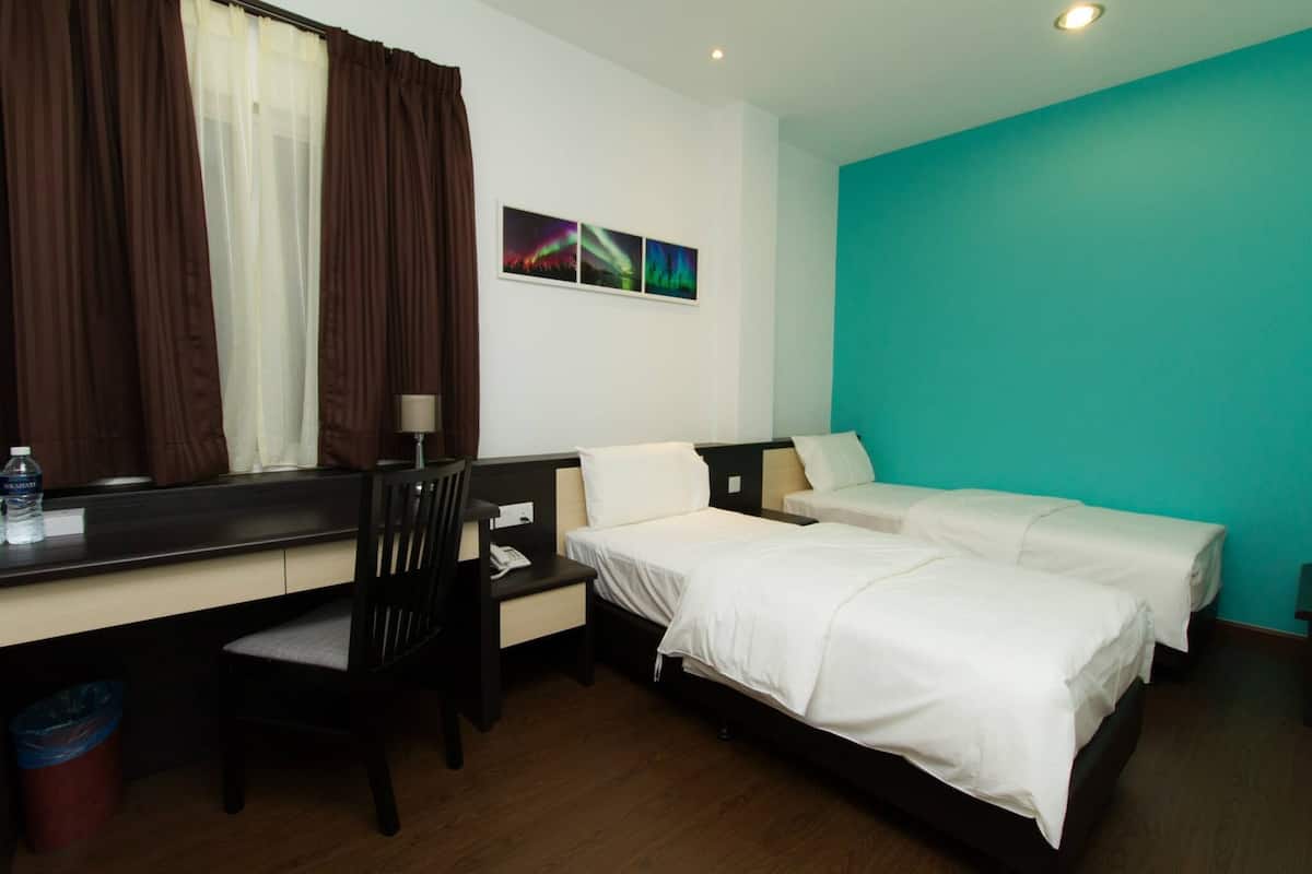 A hotel room with a desk, two beds, a chair, a trash bin, and a window with curtains.