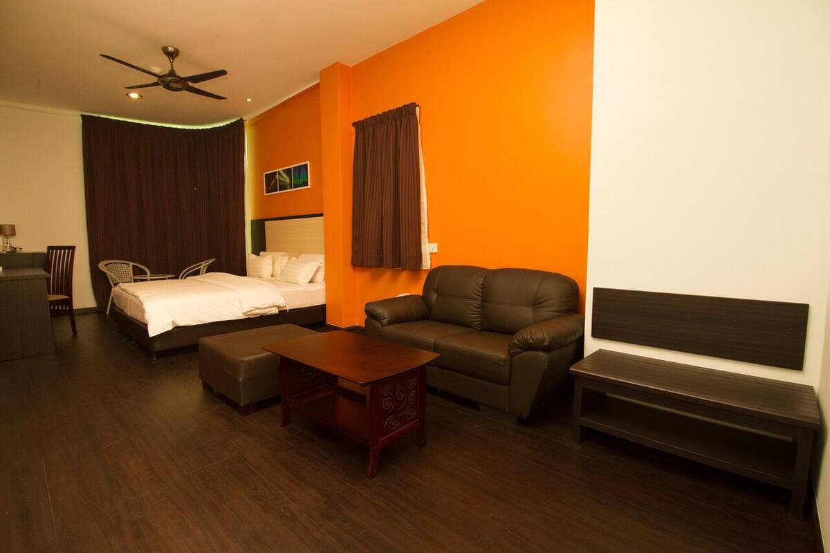 A hotel room with a bed, a sofa, a coffee table, a bench, a ceiling fan, and a large window with curtains.